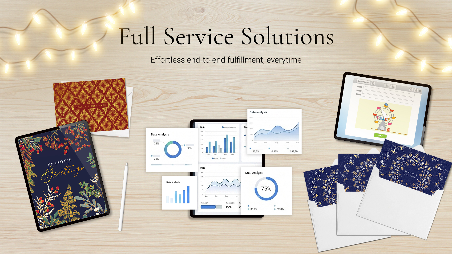 Light wood desk with holiday cards, envelopes, a tablet showing Season's Greetings, charts, and a laptop composing a holiday eCard representing Full Service Solutions